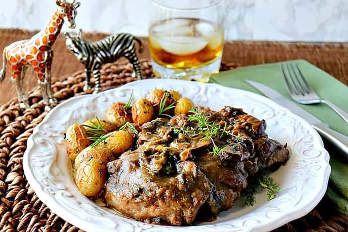 Steak with Bourbon Mushroom Sauce on a white plate with a glass of bourbon with ice in the background.