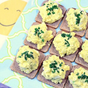 A group of Egg Salad Canapes topped with chives on a blue and yellow plate.