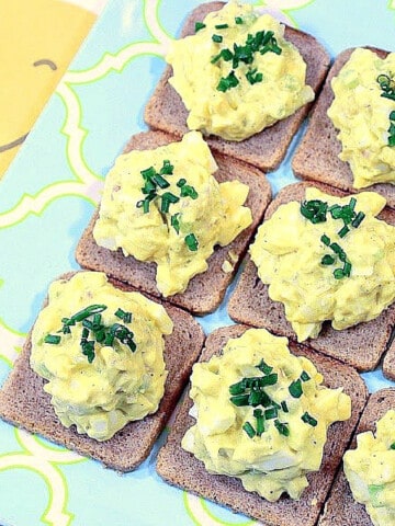 A group of Egg Salad Canapes topped with chives on a blue and yellow plate.