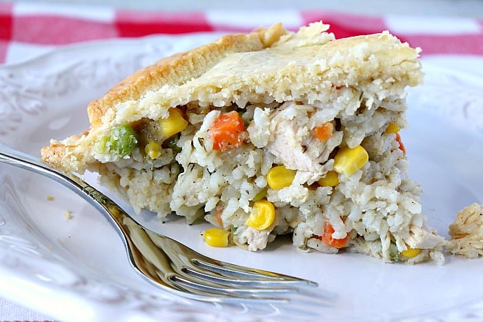 A closeup slice of a savory chicken pot pie on a white plate with a fork.