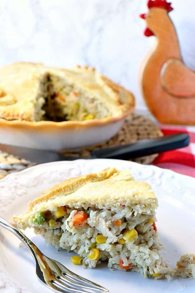 A slice of chicken and rice pot pie in the foreground and a whole pie in the background.