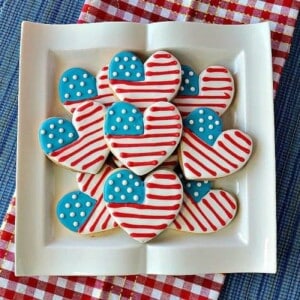 A square white plate filled with American Flad Heart Sugar cookies.