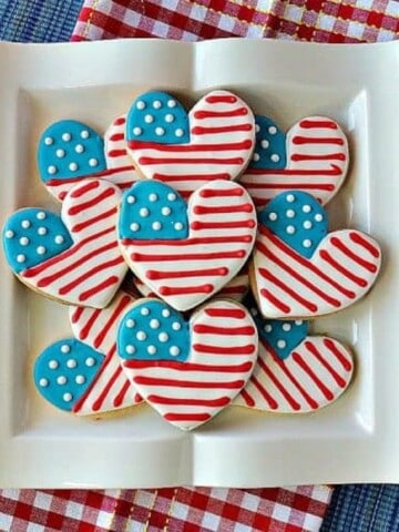 A square white plate filled with American Flad Heart Sugar cookies.