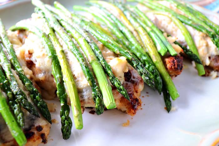 Closeup picture of breaded chicken breasts with Swiss cheese, crabmeat, and fresh asparagus spears.