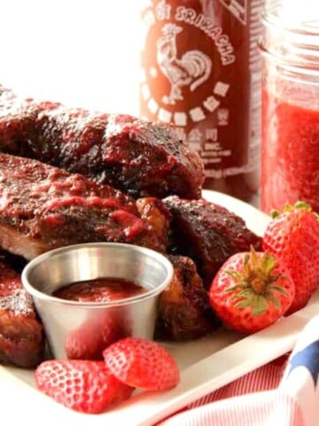 Ribs on a white plate along with Strawberry Sriracha BBQ Sauce.