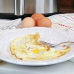Two Air Fryer Fried Eggs on a white plate with eggs in the background.