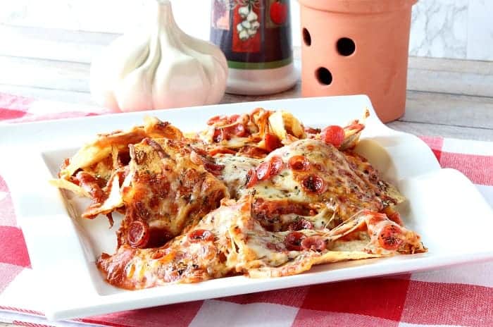 A pile of pepperoni pizza nachos on a white plate with a red and white check tablecloth.