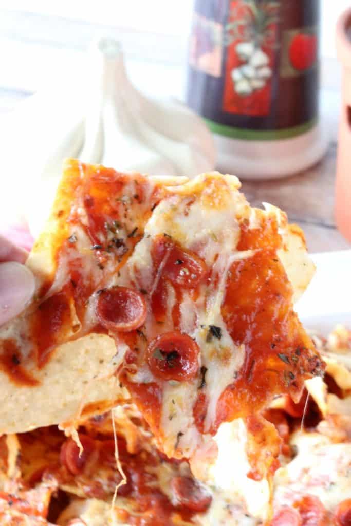 Vertical image of a pizza nachos being lifted off a plate.