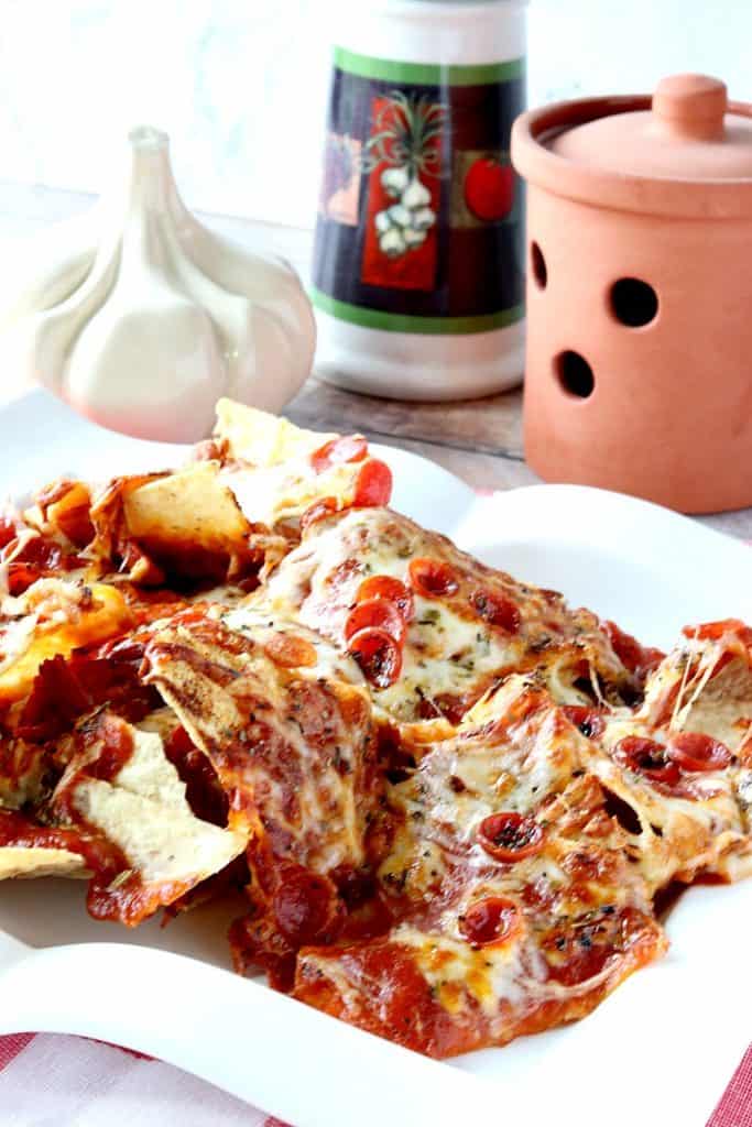 A vertical closeup photo of a pile of pepperoni pizza nachos on a square white plate.