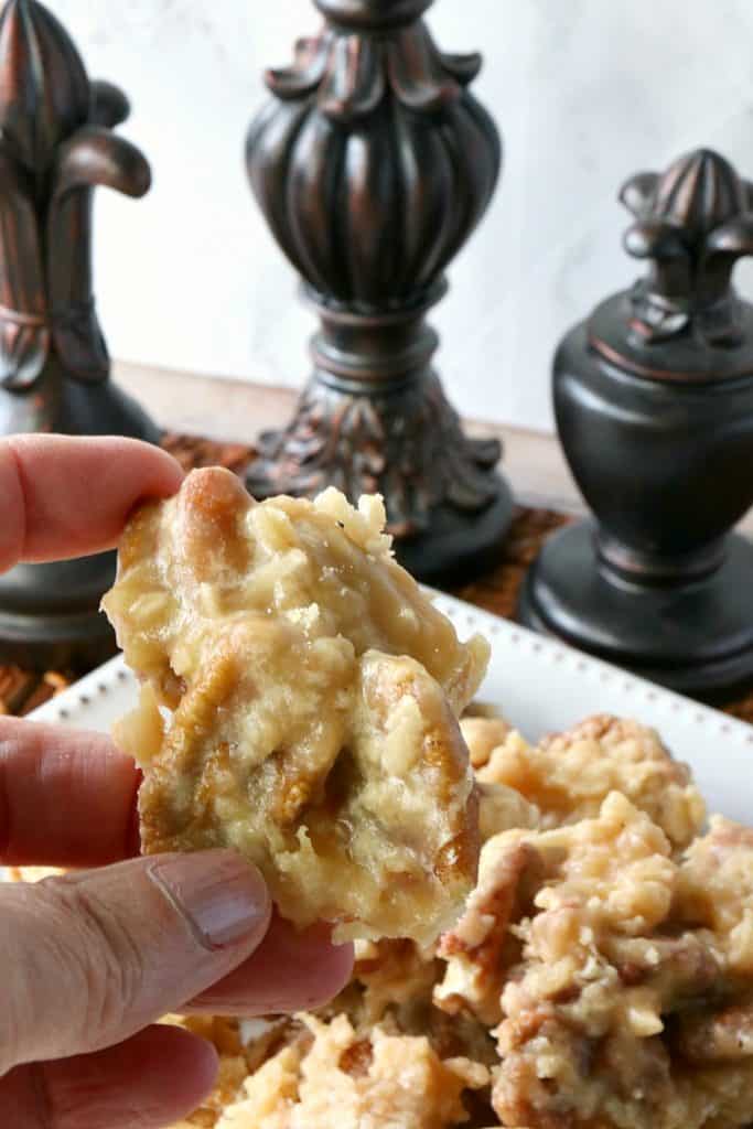 A closeup photo of one piece of pecan praline candy being held by a hand.