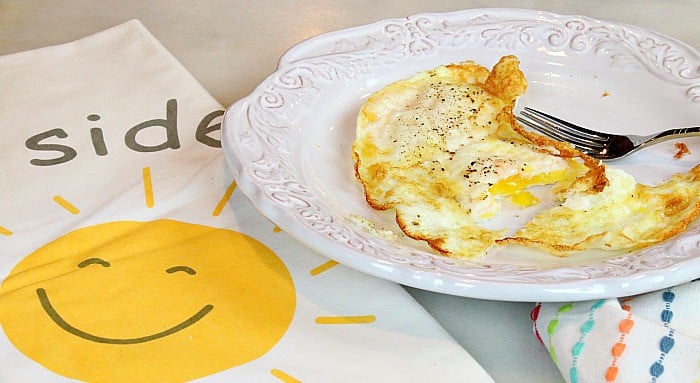 Smiling sunshine napkin and a white plate with air fryer fried eggs and a fork.