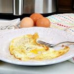 Fried eggs on a white plate with a fork and an air fryer in the background