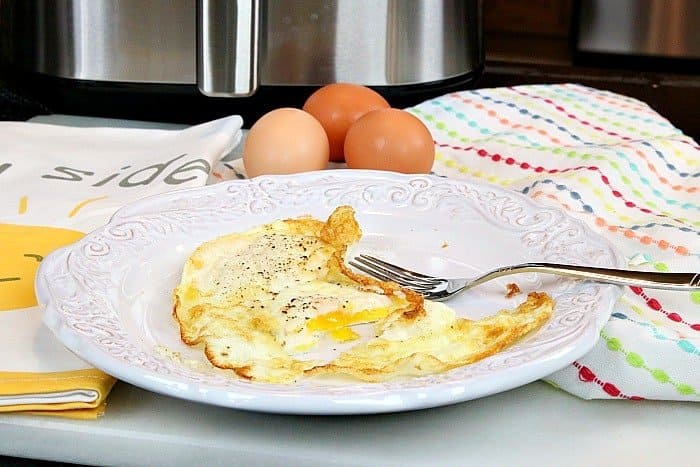 Fried eggs on a white plate with a fork and an air fryer in the background