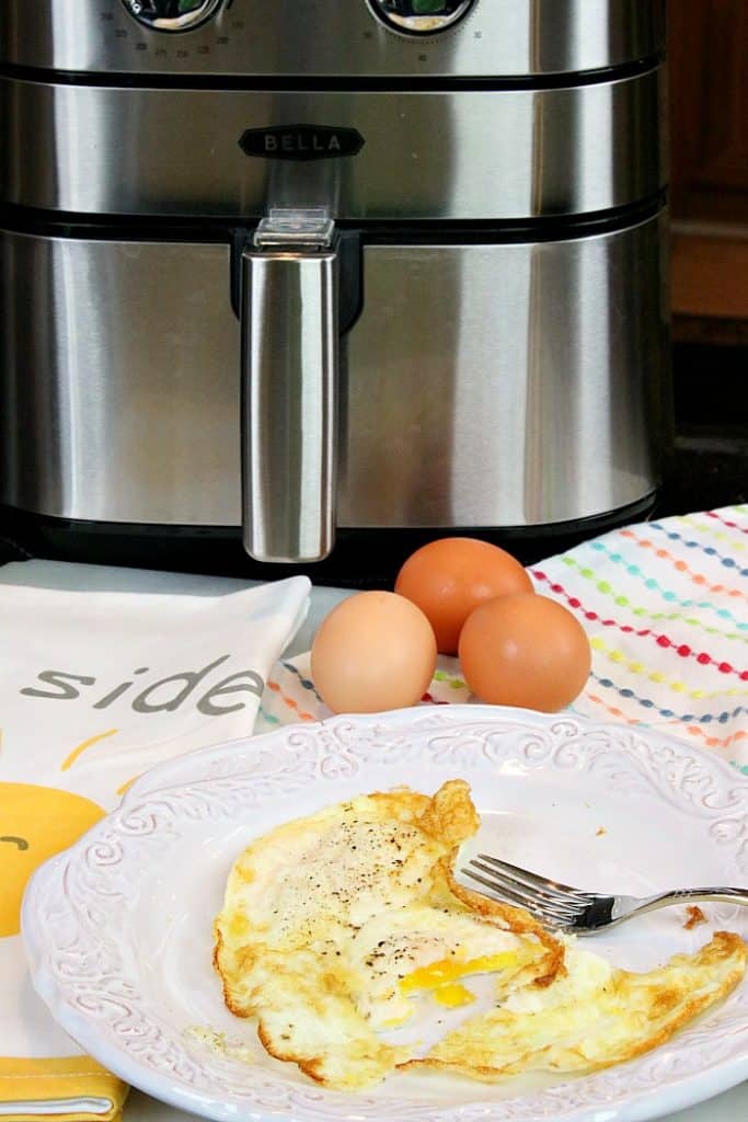 vertical photo of fried eggs on a white plate with an air fryer in the background