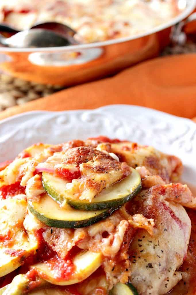 Closeup vertical photo of Italian Zucchini Parmesan on a white plate with sauce and cheese.