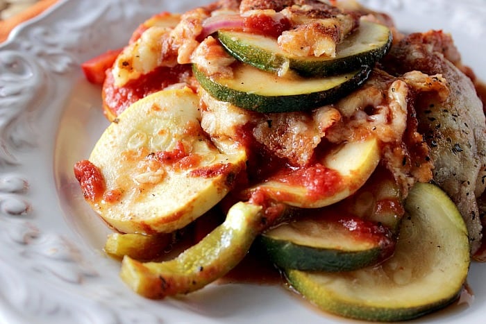 Closeup photo of Italian Zucchini Parmesan on a white plate with cheese and seasonings.