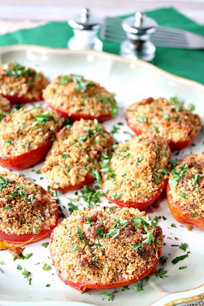 A plate of roasted tomatoes with breadcrumbs and Parmesan cheese topping with a salt and pepper shaker in the background.