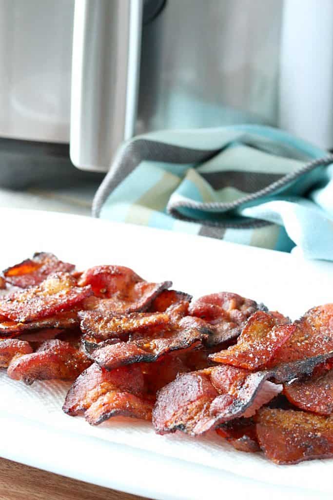 A plate piled with air fryer fried bacon and an air fryer in the background.