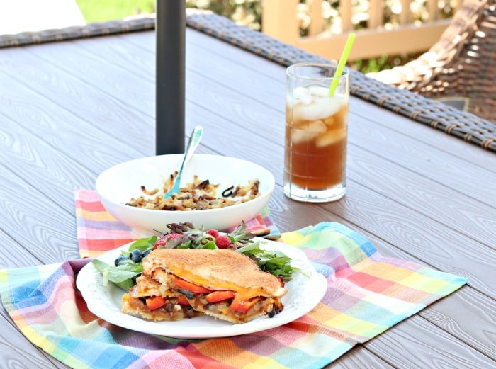 A grilled cheese sandwich on a picnic table with a glass of iced tea and colorful napkin.