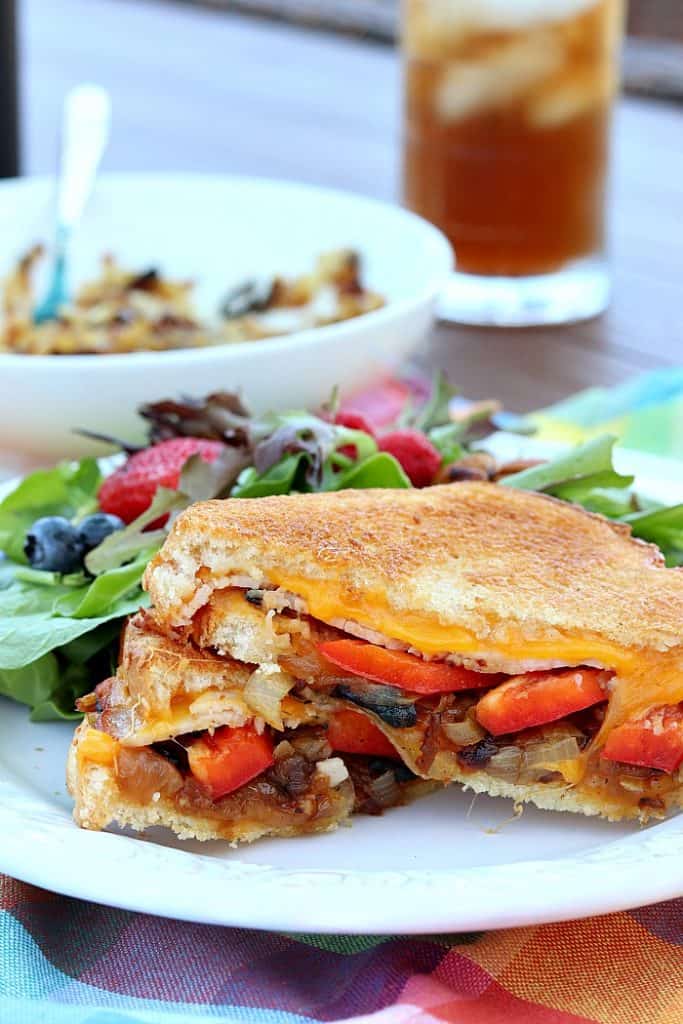 Vertical photo of a deluxe air fry grilled cheese sandwich with red pepper, caramelized onions, melted cheese, and grilled bread on a white plate.