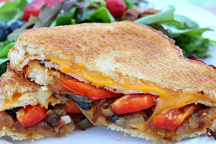 closeup photo of a grilled cheese sandwich cut in half with caramelized onions and red bell pepper.