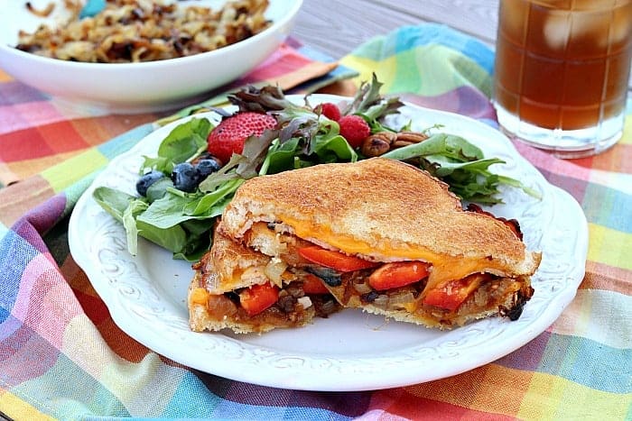 Grilled cheese sandwich with red bell pepper on a picking table with a salad on a plate.