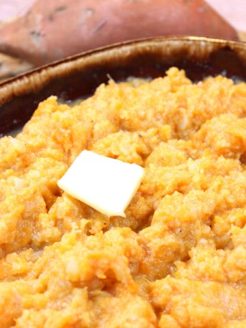 A brown serving bowl filled with Cauliflower Sweet Potato Mashers and a pat of butter.