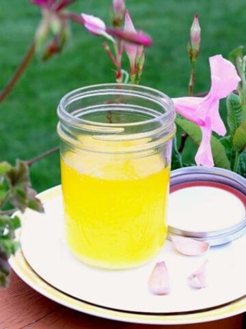 A glass mason jar filled with Homemade Garlic Ghee outside with pink flowers and green grass in the background.