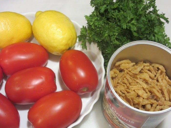 Plum tomatoes and lemons in a dish with French fried onions and parsley on the side.