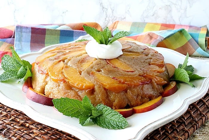 A whole nectarine upside down cake on a square white plate with mint sprigs and a dollop of whipped cream.