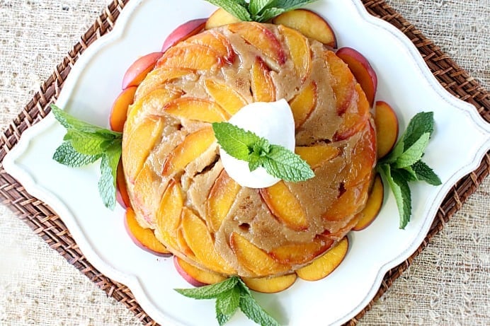 Overhead photo of a nectarine fruit cake on a square white plate garnished with mint, whipped cream and nectarine slices.