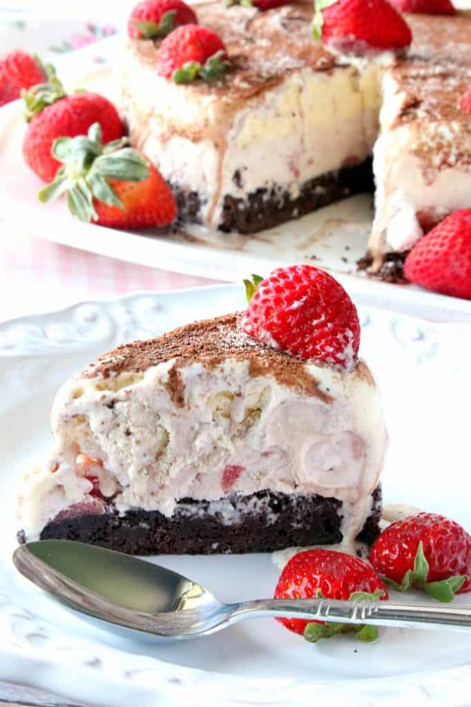 A slice of a neapolitan ice cream cake with a brownie bottom and strawberries.