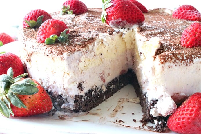 A Neapolitan Ice Cream Cake on a plate with a slice taken out and a strawberry garnish.