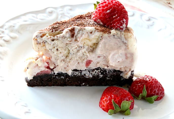 A single slice of Neapolitan ice cream cake on a white plate with a strawberry garnish.