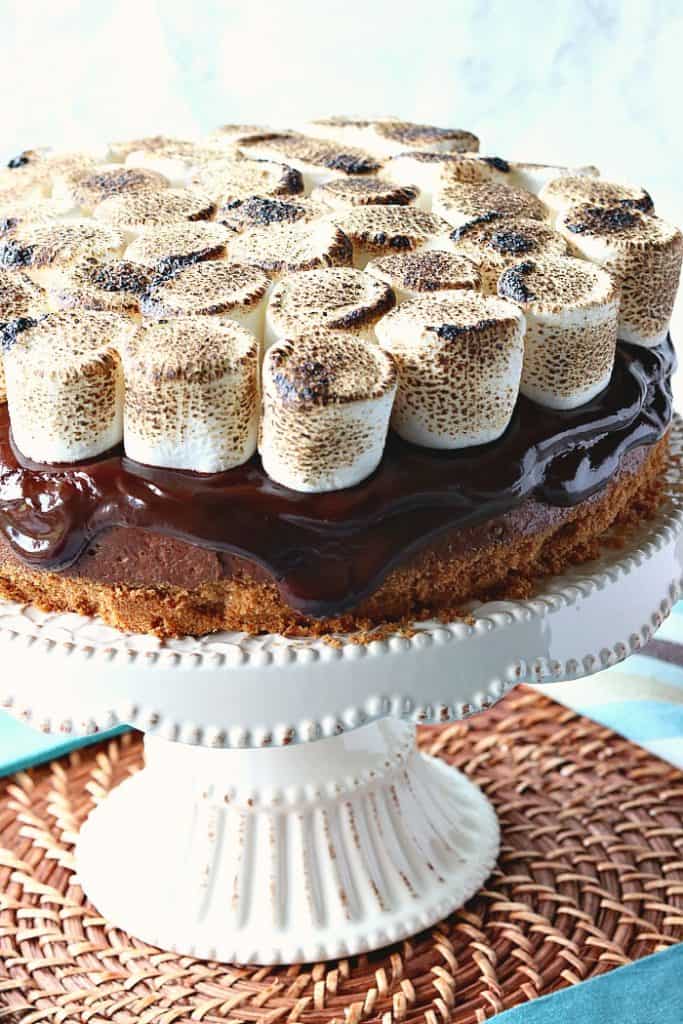 A closeup of a s'mores cheesecake with chocolate ganache and toasted marshmallows on top.