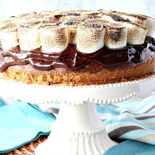 S'mores cheesecake on a cake stand with blue napkins in the background