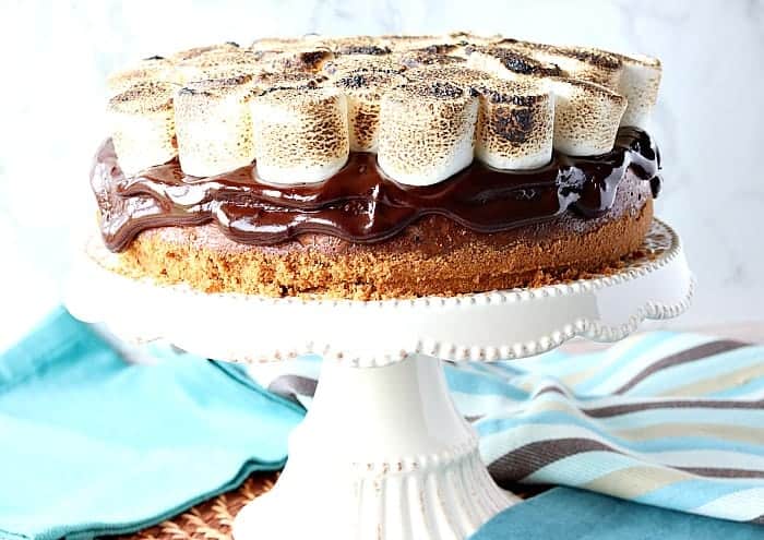 S'mores cheesecake on a cake stand with blue napkins in the background. Romantic chocolate dessert recipes collection.