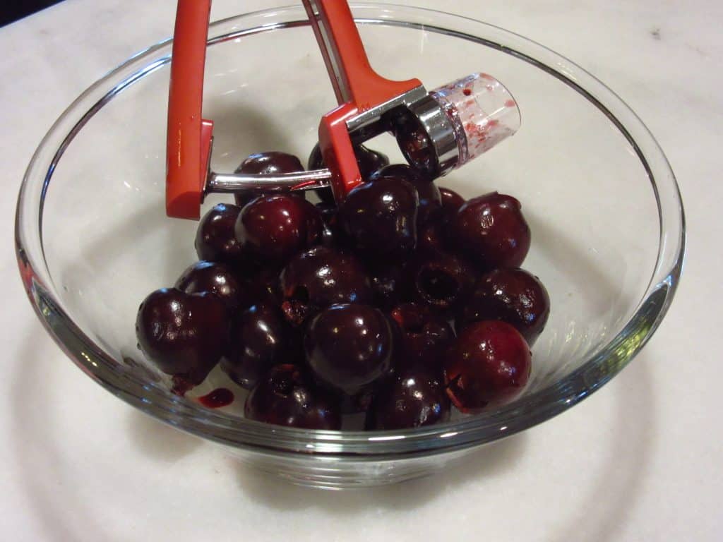 Glass bowl of fresh cherries with a cherry pitter.