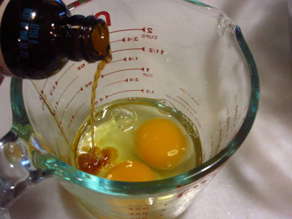 Two eggs and vanilla extract in a glass measuring bowl.