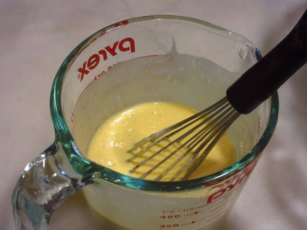 A whisk in a measuring bowl with eggs.