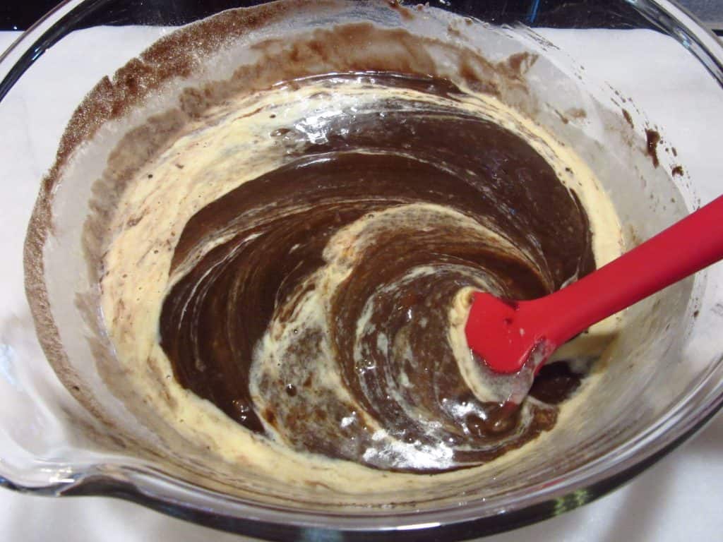 A red spatula mixing the ingredients for a chocolate cherry Bundt cake.
