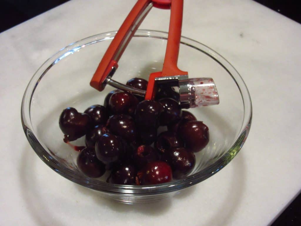A glass bowl filled with cherries along with a cherry pitter.