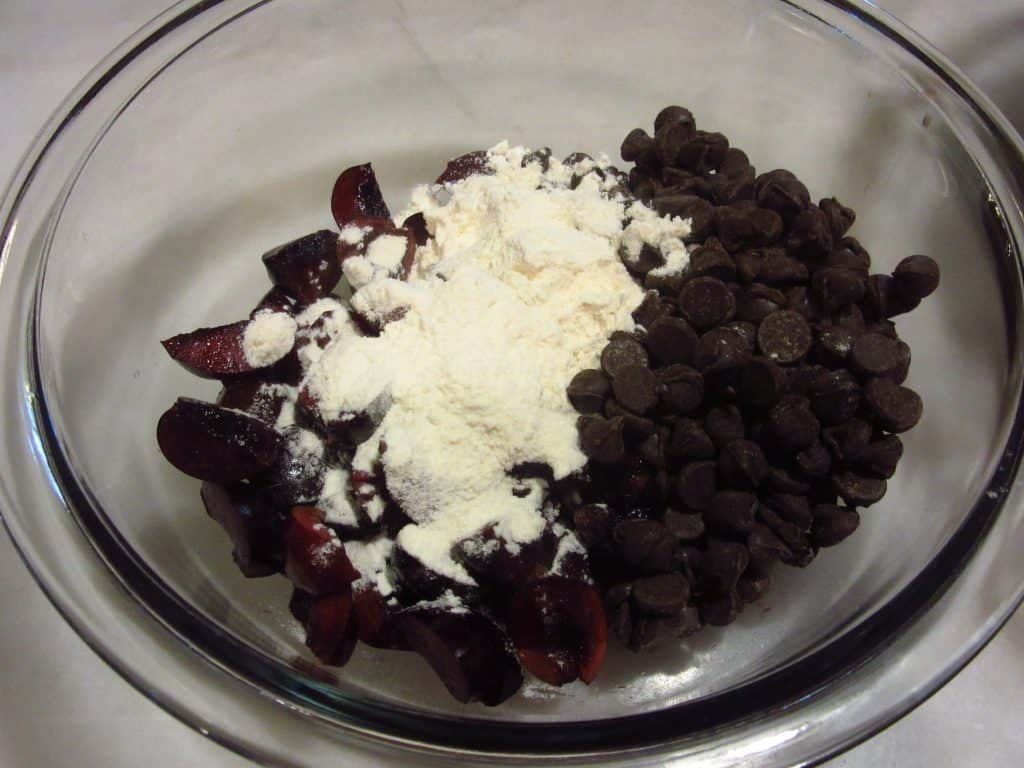 Pitted, chopped cherries along with chocolate chips in a bowl with flour.