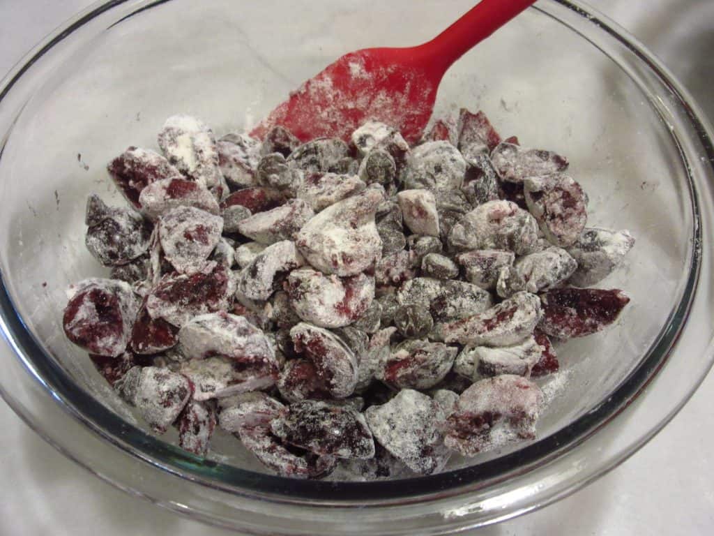 A glass bowl filled with floured chocolate chips and cherries.