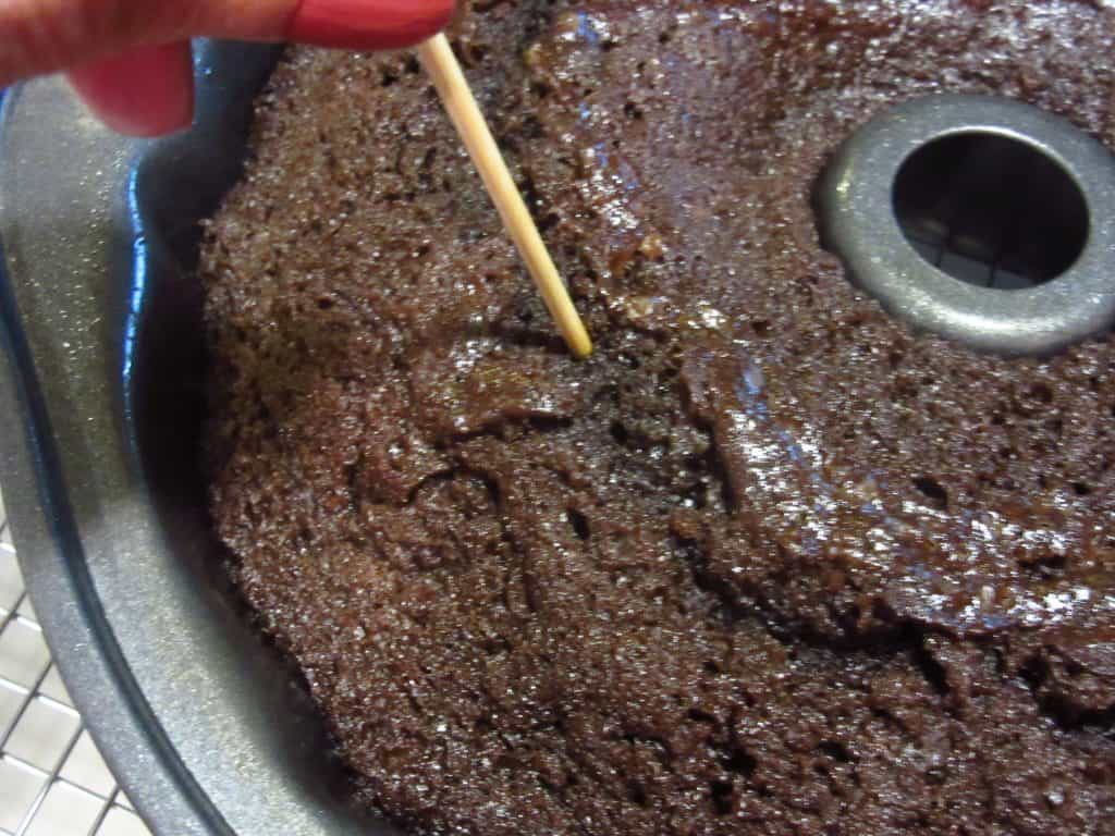 A tooth pick checking the doneness of a chocolate cherry Bundt cake.