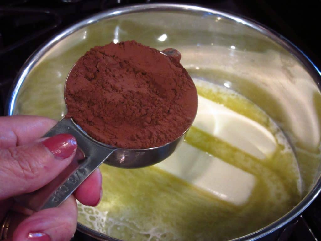 Cocoa powder being added to a saucepan with melted butter.