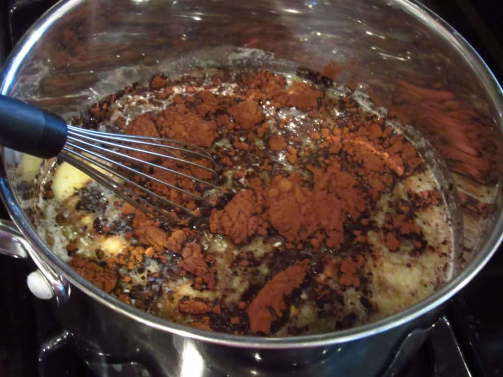 Cocoa powder being whisked into melted butter in a saucepan.