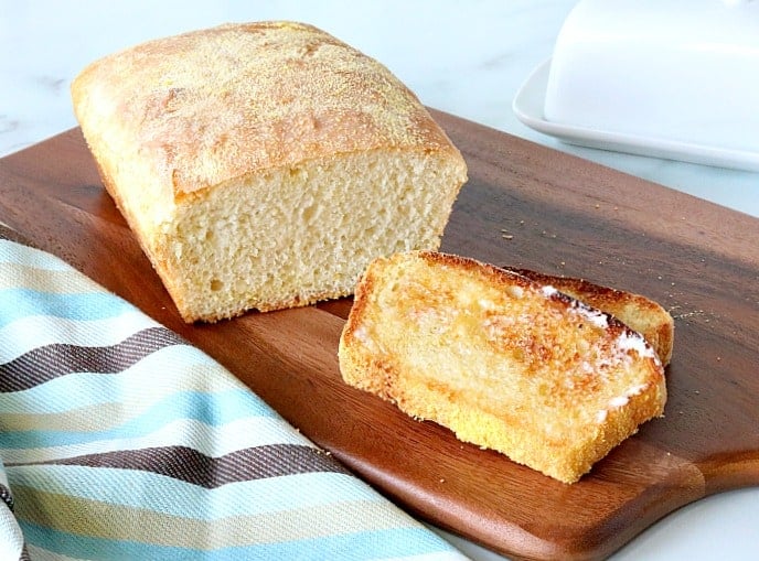 A slices loaf of English muffin bread on a wooden board with a blue and brown striped napkin.