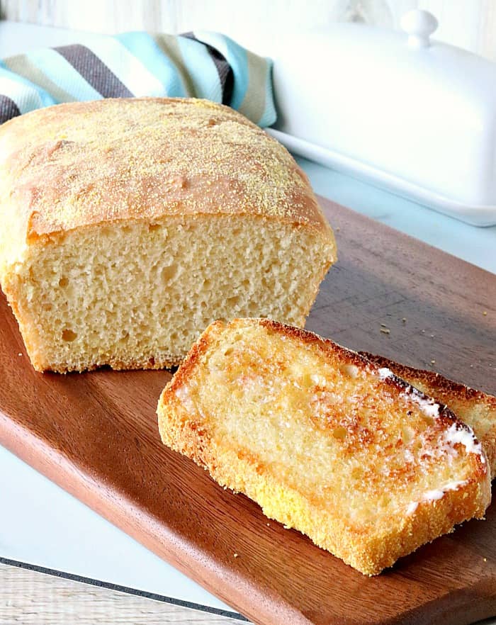 A vertical photo of a sliced loaf of English muffin bread with two toasted slices.