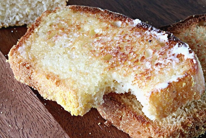 A toasted slice of homemade English muffin bread with butter and a bite taken out.
